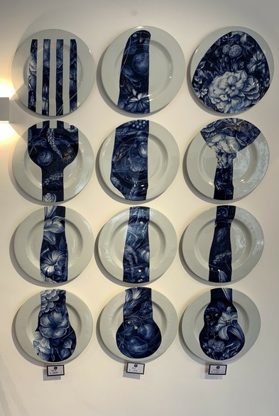 12 plates hanging on a wall in a 3 x 4 pattern, the left four column having a blue pattern of a fork split across them, the middle four, a knife, the right four a spoon 